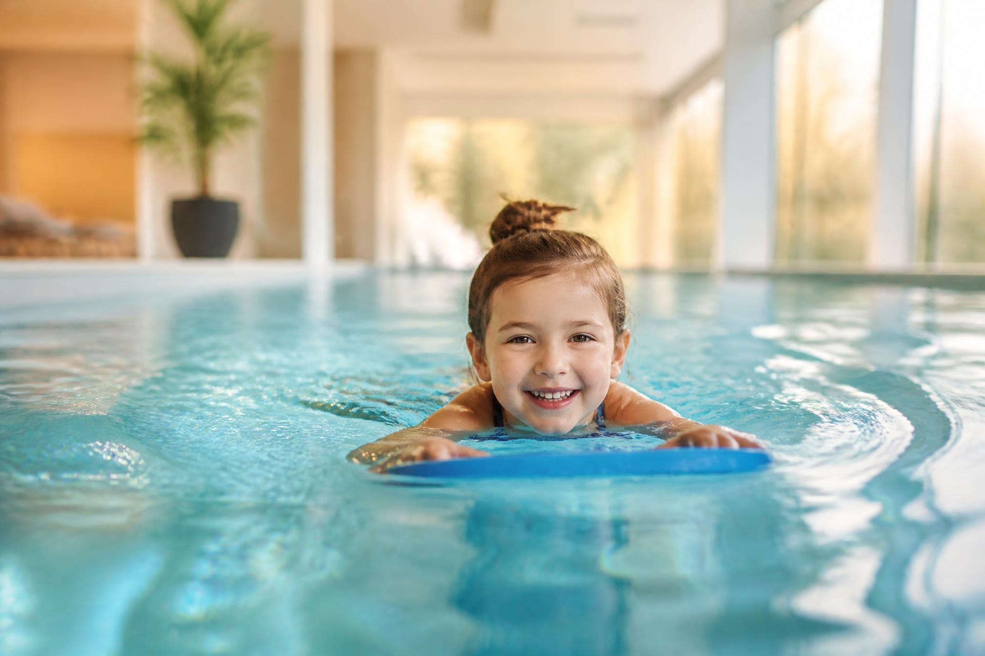Young child smiling with a kickboard in a warm, clean private pool